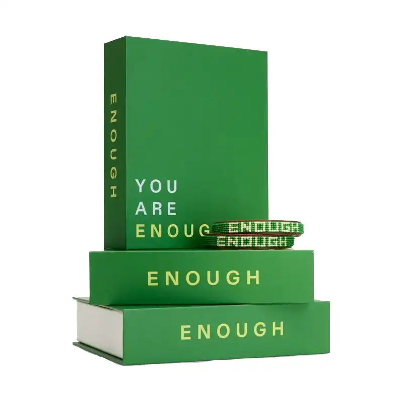 A green book-shaped box with the word 'ENOUGH' printed on the cover, displayed stacked on top of two matching green boxes.